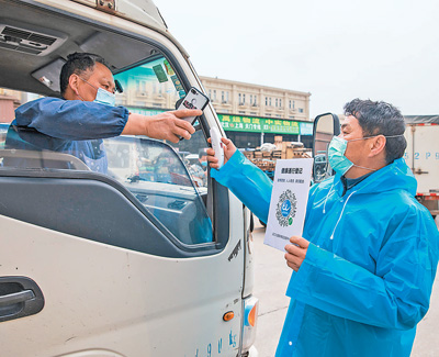 汉口北物流园,工作人员为进站人员测量体温,并指导其扫码实名登记.